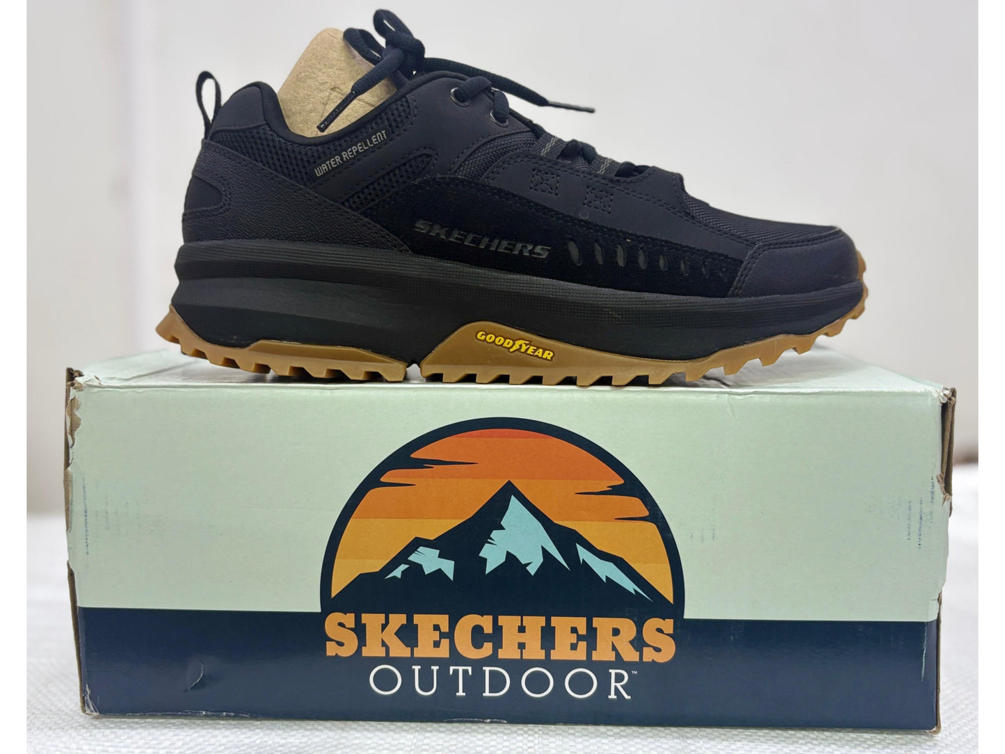 Side view of a black Skechers Outdoor walking shoe with gum Goodyear outsole and water-repellent upper, resting on Skechers Outdoor box
