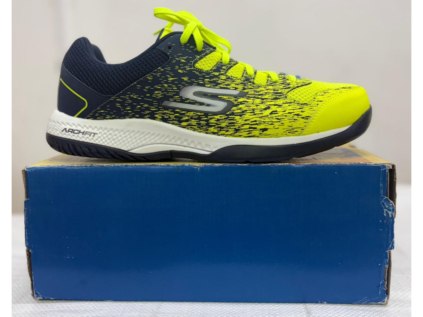 Navy and neon yellow Skechers Arch Fit athletic shoe with white midsole on blue shoebox.