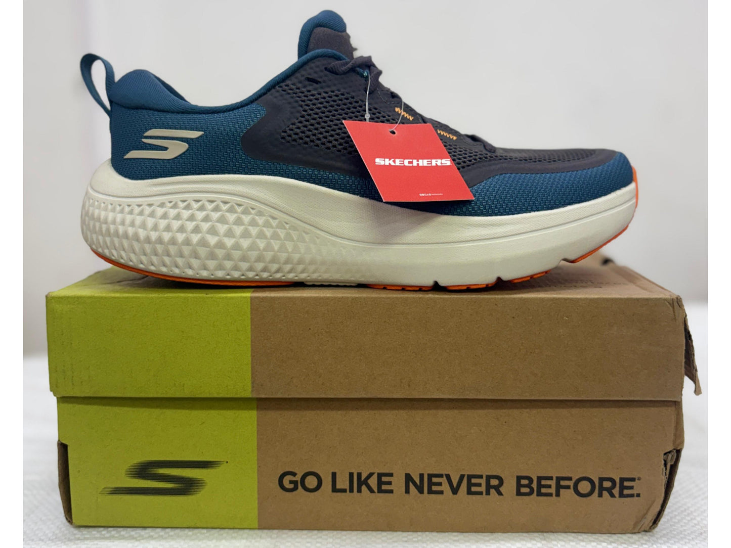 Side view of a navy and teal Skechers GO RUN shoe with orange outsole accents and chunky white midsole