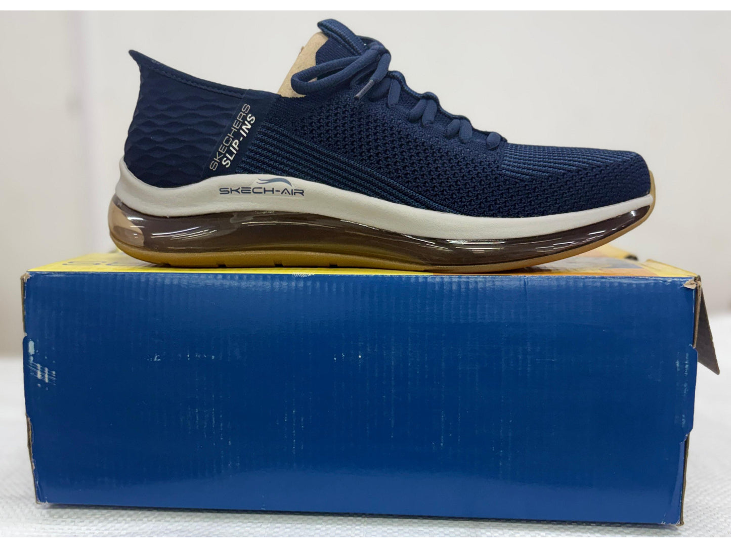 Navy Skechers Slip-ins sneaker with amber Skech-Air heel unit and gum outsole on blue box.