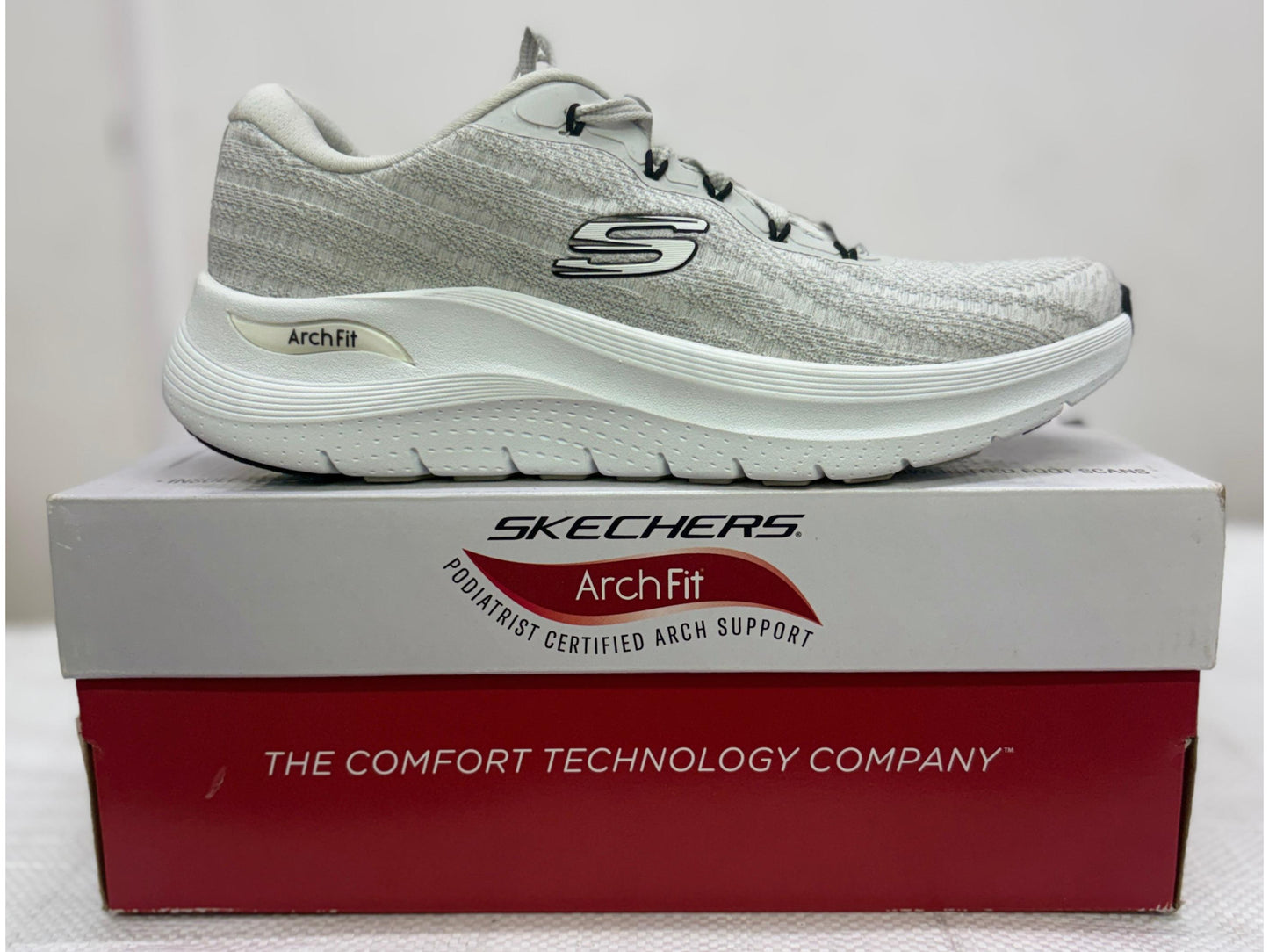 Side profile of a grey Skechers Arch Fit walking shoe with white cushioned midsole on Arch Fit branded box