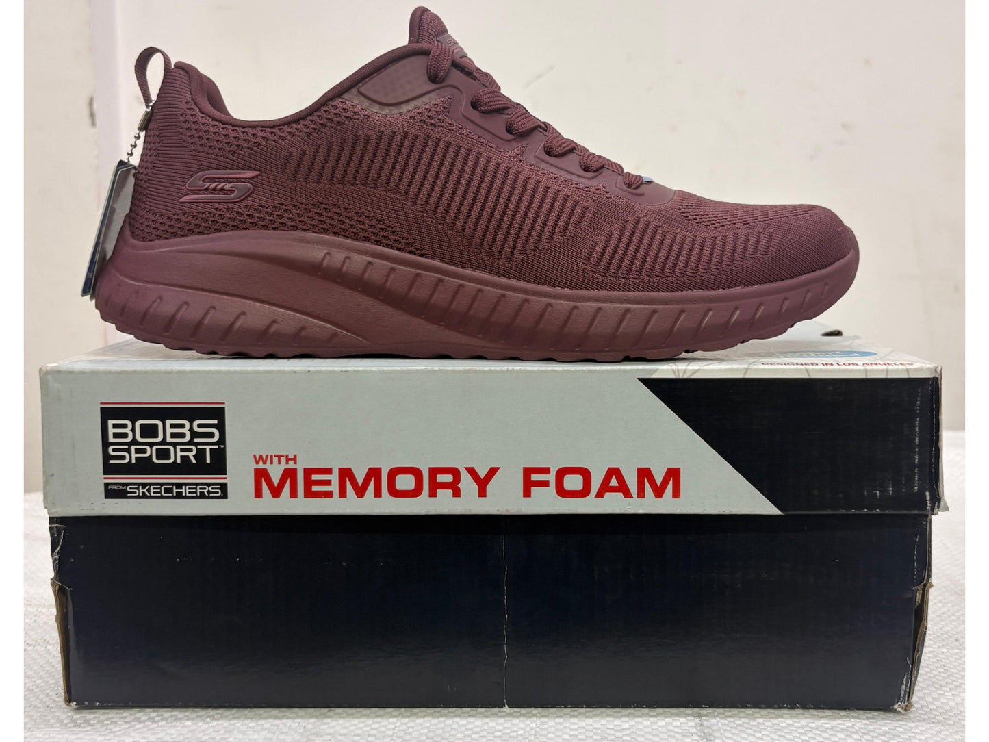 Side view of a monochromatic burgundy Skechers BOBS Sport knit sneaker with memory foam branding on box