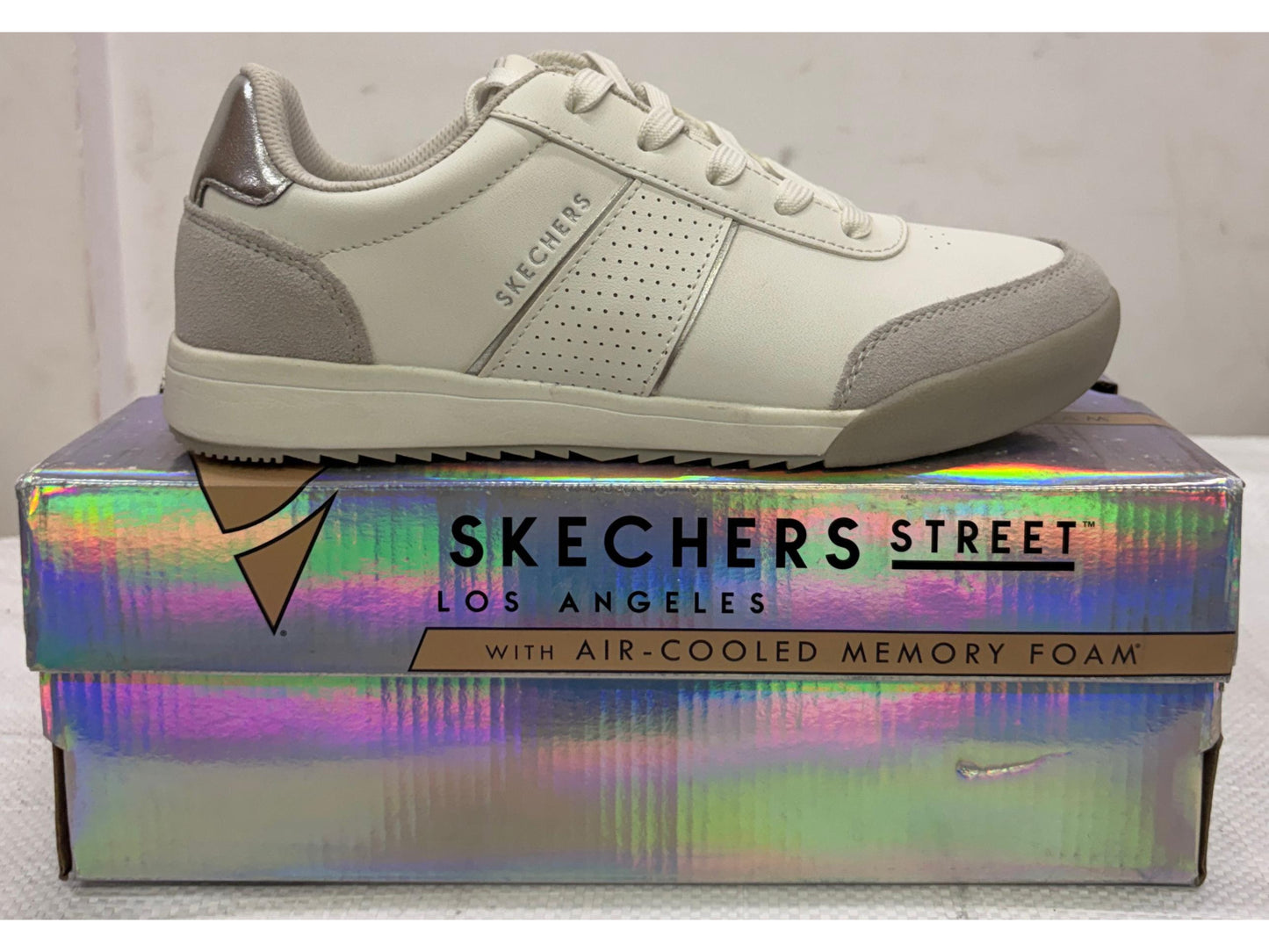 Side view of an off-white Skechers Street Los Angeles sneaker with beige suede overlays and silver heel tab