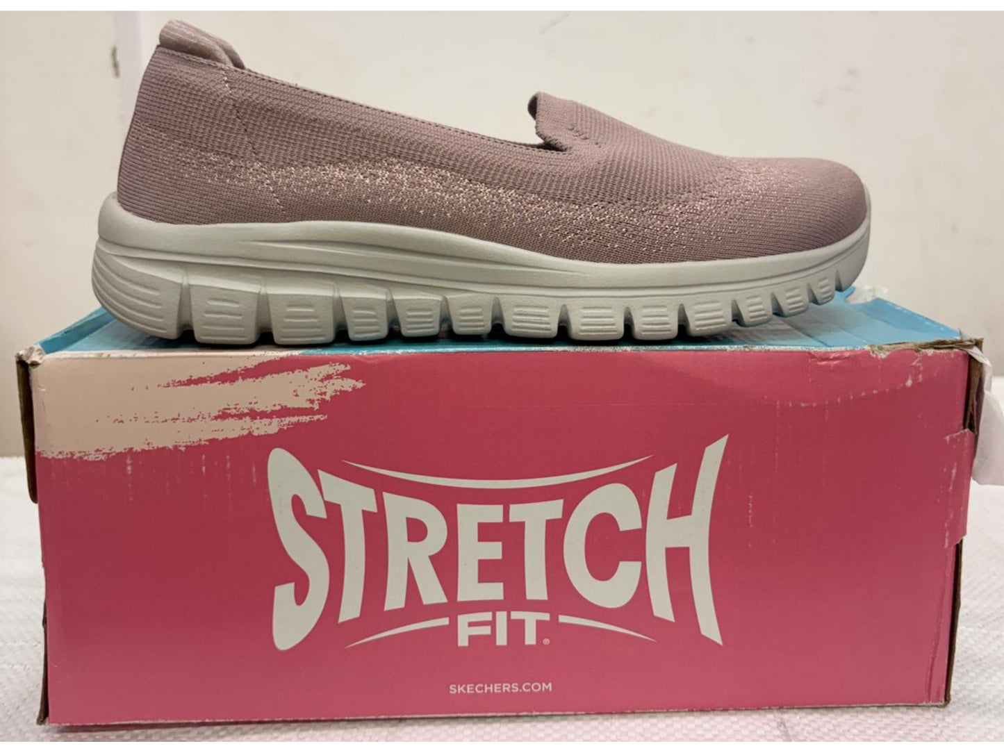 Dusty pink Skechers Stretch Fit slip-on walking shoe with light grey cushioned sole on pink retail box.